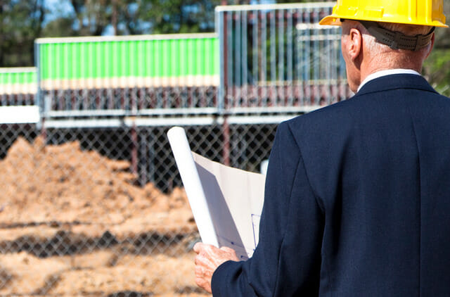 real estate professional looking at plans at construction site for retailer