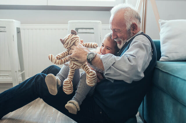 grandfather playing with granddaughter holding stuffed animal on floor